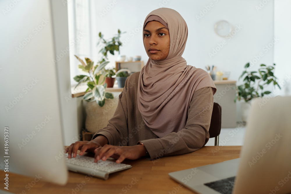Aufkleber Young serious female programmer looking at computer screen while analyzing or decoding data or developing new software by workplace