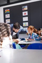 Vertical of diverse male teacher helping girl at her desk in elementary school classroom, copy space