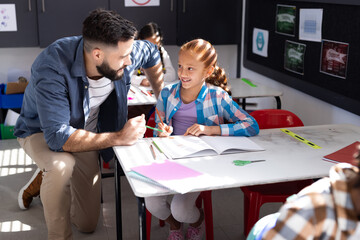 Diverse male teacher and smiling girl at desk in elementary school class, copy space