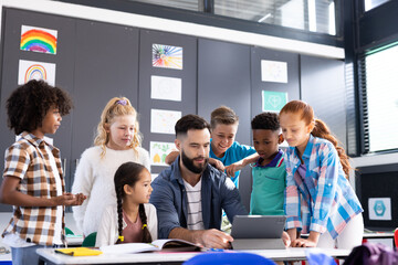 Diverse elementary schoolchildren and male teacher using tablet together in classroom, copy space