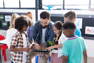 Diverse elementary schoolchildren and male teacher using wind turbine and tablet in classroom