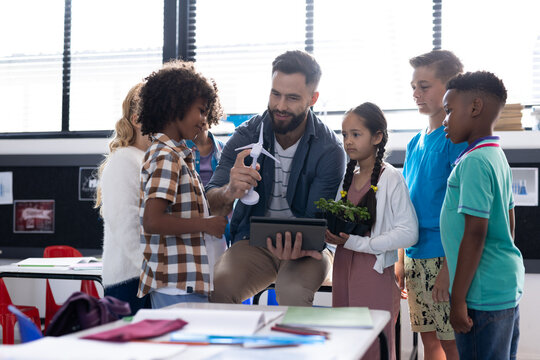 Diverse elementary schoolchildren and male teacher looking at wind turbine in classroom, copy space