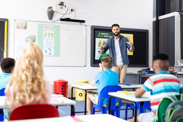 Caucasian male teacher addressing pupils in diverse elementary school classroom, copy space