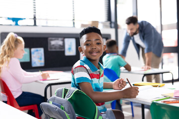 Obraz premium Portrait of smiling african american boy at desk in elementary school classroom, copy space