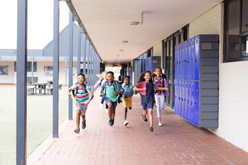 Diverse, happy children with schoolbags running in elementary school corridor, copy space