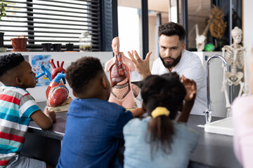 Diverse elementary school pupils and male biology teacher studying human body model, copy space