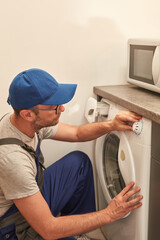 Handyman fixing broken washing machine in the apartment.