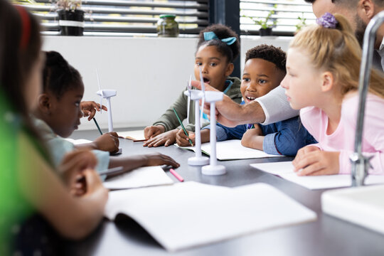 Diverse elementary schoolchildren and male teacher studying wind turbines in class, copy space