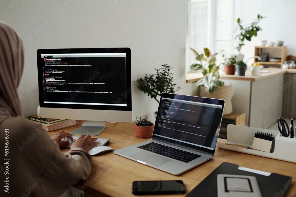 Poster Young Muslim woman in headscarf decoding data or developing new software while typing on computer keyboard by workplace in home office