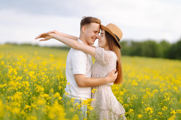 Young couple in love walks through a rapeseed field. Happy men and women in style enjoy the time spent together. The concept of love, test, relationship.