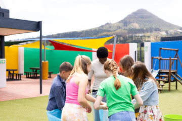 Diverse female teacher and pupils collecting rubbish for recycling in schoolyard, with copy space
