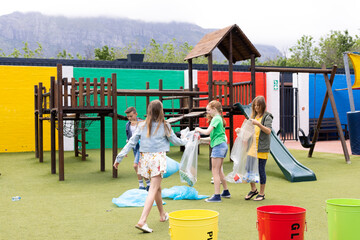 Group of caucasian schoolchildren collecting rubbish for recycling in schoolyard, with copy space