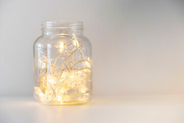 Warm glowing christmas lights in a glass jar on a white background