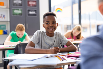Portrait of smiling african american schoolboy working at his desk in class, copy space