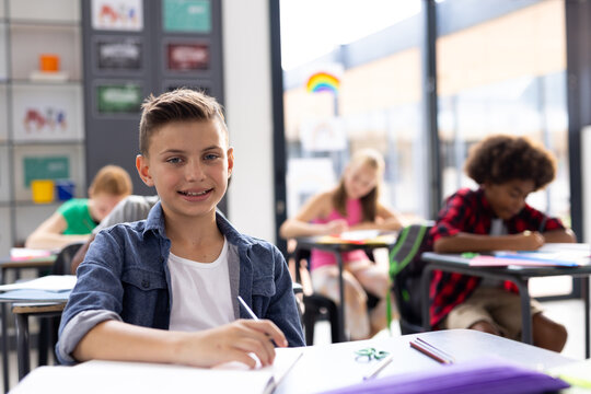 Portrait of smiling caucasian schoolboy working at his desk in class, with copy space - Powered by Adobe