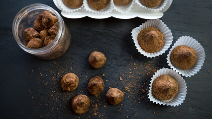 Truffle candies liberally sprinkled with cocoa in white substrates on a black tray.