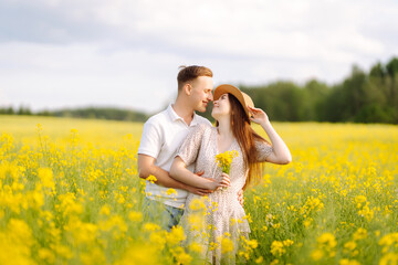 Young couple in love walks through a rapeseed field. Happy men and women in style enjoy the time spent together. The concept of love, test, relationship.