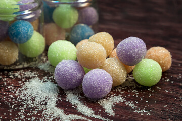 Colored round candy balls sprinkled with sugar in a glass jar and wooden table.