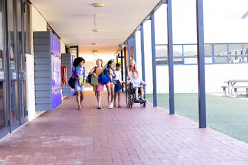 Diverse group of school children walking in school corridor talking, one in wheelchair, copy space