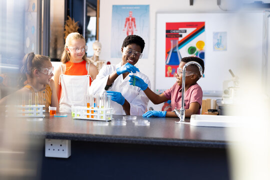 Happy diverse female teacher and school children doing experiment in chemistry class