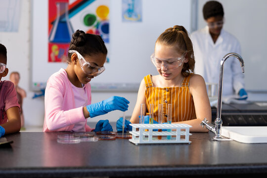 Two happy diverse schoolgirls doing an experiment in chemistry class