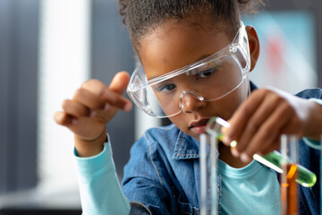 Serious biracial schoolgirl in safety glasses doing experiment in science class with copy space