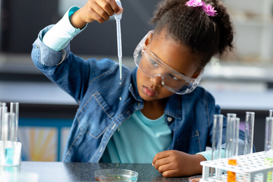 Biracial schoolgirl in safety glasses using pipette in science class with copy space