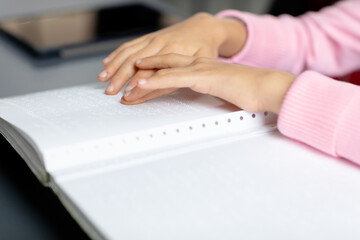 Hands of blind, biracial schoolgirl at desk reading braille in class with copy space