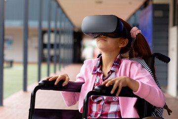 Happy biracial schoolgirl in wheelchair, using vr headset in school corridor