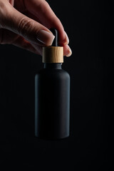 Female hand holding a bottle with serum for face care. Daily routine and treatment for the skin. Mockup for your design, dark mood, deep shadows