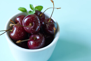 Cherries in a bowl with water drops on a blue background