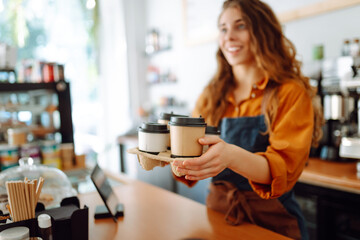 Best coffee for you. Cheerful woman in an apron at the bar counter holds coffee glasses in a cafe. Takeaway food concept.