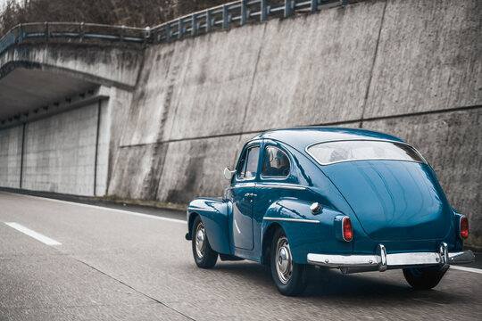 Old vintage European car model on the public highway. Blue oldtimer coupe speeding on the road.