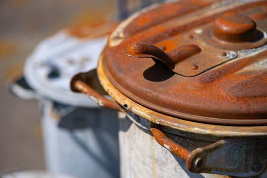 2 old historic german trash cans with rusty corroded surface. Vintage dustbins with selective focus in bright sunlight. Weathered objects from the beginnings of automatical public garbage collection.