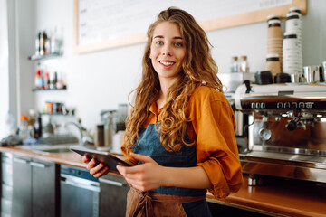 Beautiful woman owner stands behind the counter of a coffee shop. A barista with a digital tablet takes an order. Business concept. Takeaway food.