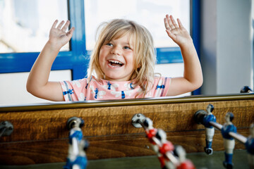 Little preschool girl playing table soccer. Happy excited positive child having fun with family...
