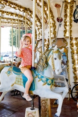 Happy positive preschool girl having a ride on the old vintage merry-go-round in city of St Malo...
