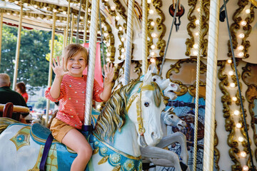 Happy positive preschool girl having a ride on the old vintage merry-go-round in city of St Malo...
