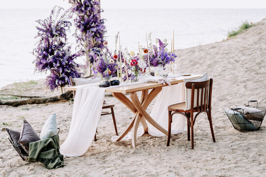 Dining Table and Chairs on Sandy Beach Nature Photography. Desk Decorated Natural Fresh Flowers and Plant for Celebrate Valentine Day on Seashore. Picnic Date for Lovely Couple Outside