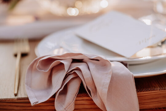 Napkin and Restaurant Card on Plate Closeup Photo. Textile Towel Accessory, Empty Ceramic Dishware with Cafe Menu and Metallic Fork Utensil on Wooden Dining Table. Buffet Catering Service