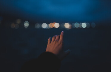 Wide shot of a pretty hand reaching up to a blurry skyline at night