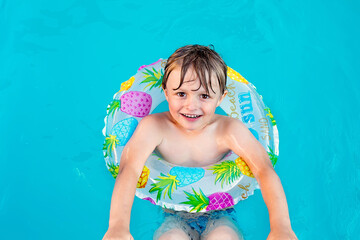 HAPPY BLOND BOY IN A LIFEBUOY SWIMMING IN THE POOL ENJOYING THE WARMTH