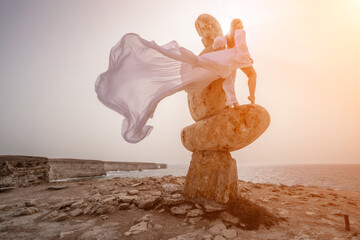 Woman sky stone. Lady stands on stone sculpture with ocean view. She is dressed in a white long...