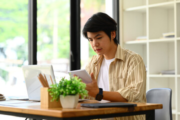 Handsome young businessman reading book or checking his working schedule plan while sitting at desk