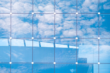 Reflection of white fluffy clouds with blue sky on rectangle pattern surface of modern glass...
