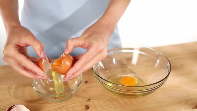 Female hands separate the yolk from the protein. Close-up. Raw egg yolk separated inside half of broken eggshell holding in fingers. Preparation of food ingredient for cooking ang baking.