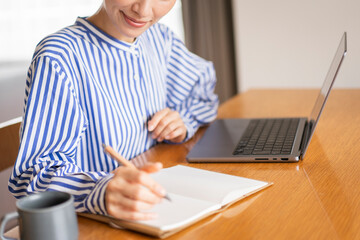 自宅でノートパソコンを開きノートに書いている女性 - obrazy, fototapety, plakaty