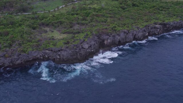 Waves crashing at rocky cliff at Sumba island during sunrise, aerial