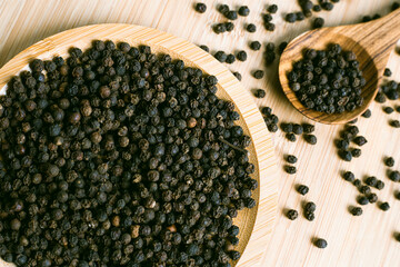 Black pepper seeds on a wooden spoon. Pile of black pepper in a wooden bowl, close up, top view.