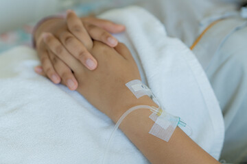 Young patient asian woman lying on the bed in hospital with IV saline drip to the back of the hand, teenager sick in hospital, Selective focus, healthcare, and health insurance concept.